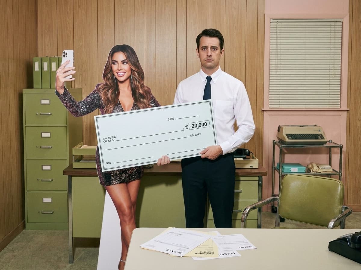 A cardboard cutout of an influencer taking a selfie beside a deadpan marketer holding an oversized $20,000 novelty check.
